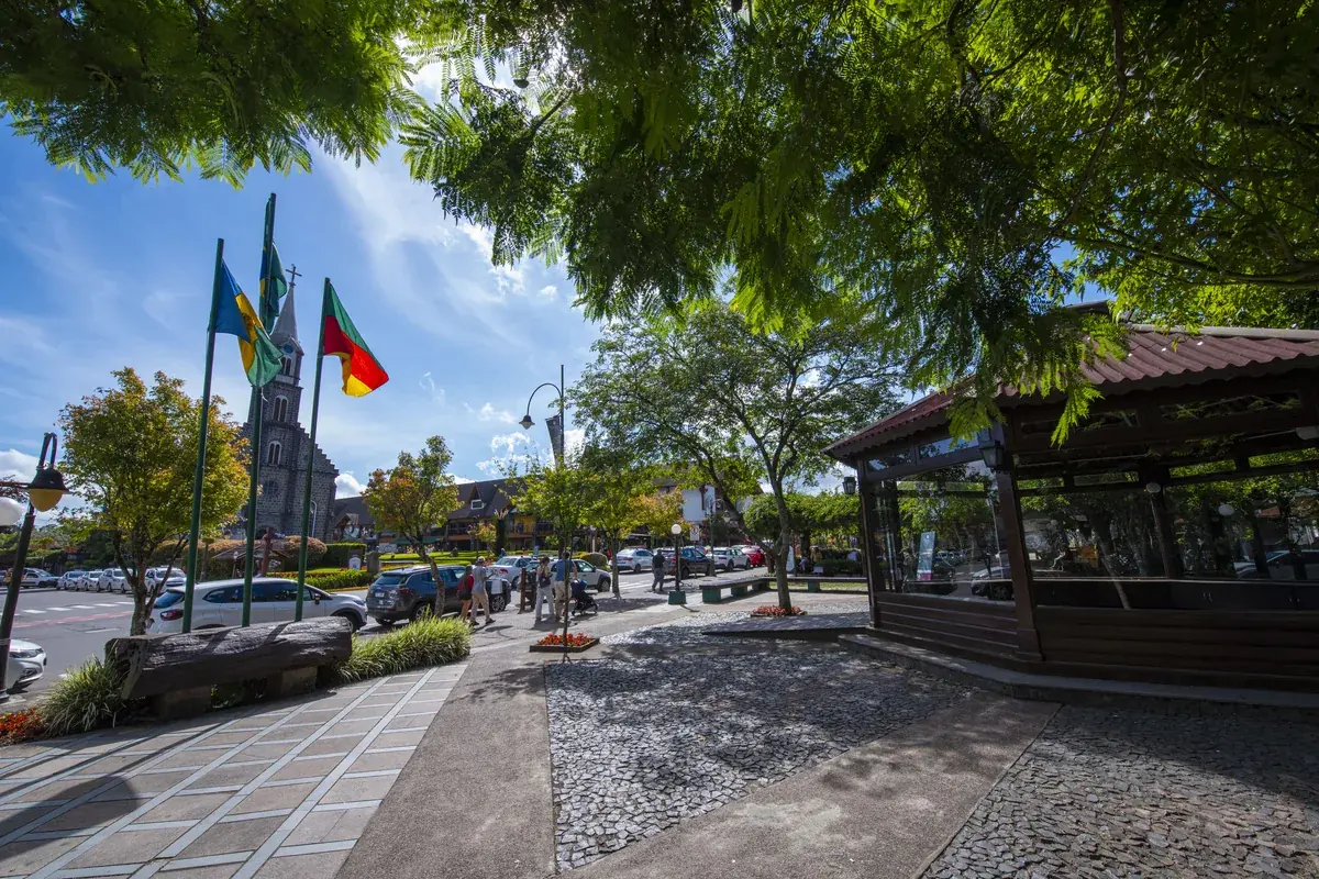 Praça central de Gramado com as bandeiras do Brasil, do Rio Grande do Sul e do município hasteadas ao lado da igreja de pedra